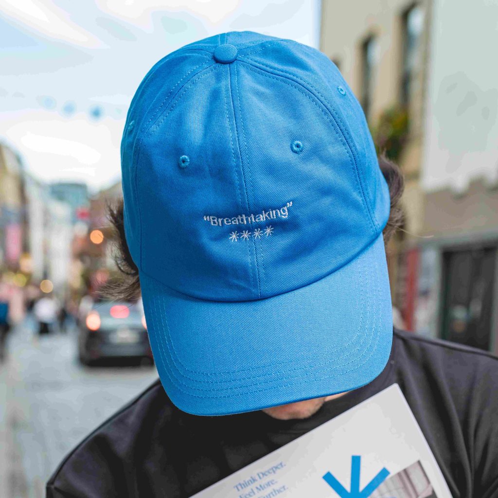 Person wearing blue cap reading Breathtaking with stars, holding a paper, on a city street.